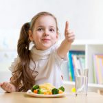 child girl eats healthy food showing thumb up