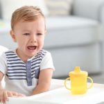 Adorable crying baby sitting in highchair at home