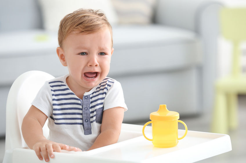 Adorable crying baby sitting in highchair at home