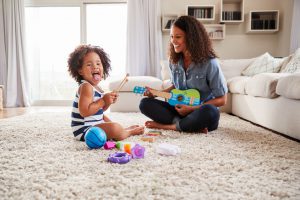 Young black mum plays ukulele with toddler daughter