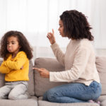 Angry Black Mother Scolding Kid Shouting At Sad Daughter Sitting On Sofa At Home. Family Quarrels And Problems