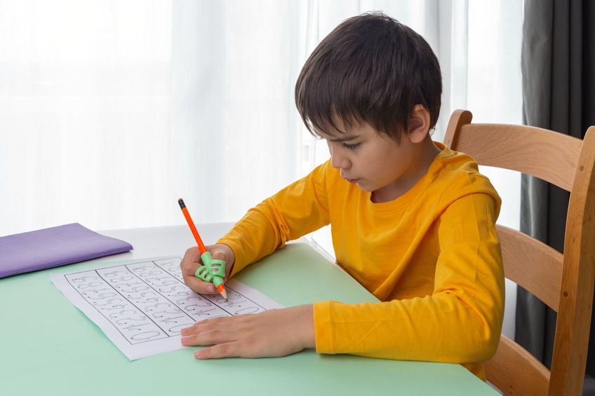child do homework, boy use ergonomic training pencil holder, correcting pencil grip